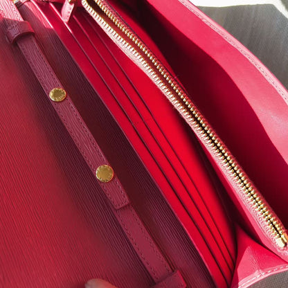 Close-up of a red leather handbag showing the interior, including a gold zipper, card slots, and a matching red strap with gold-tone rivets.