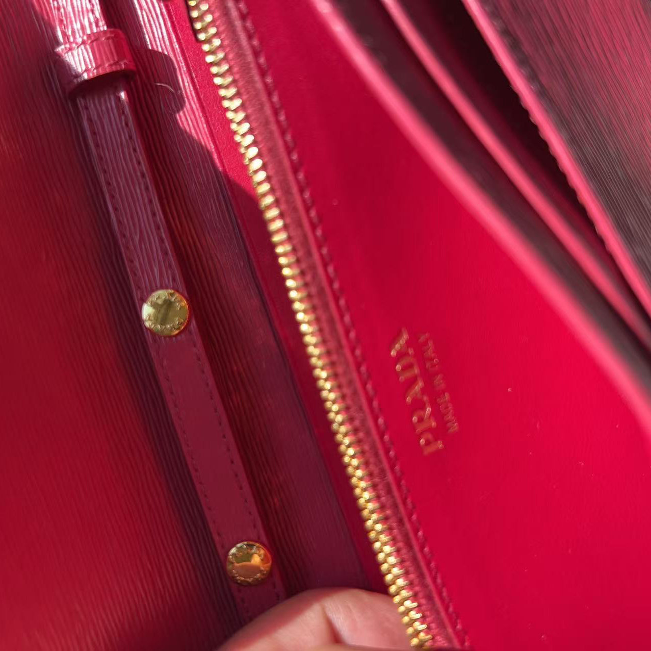 Close-up of a bright pink-red leather clutch or wallet with gold-tone hardware, a gold zipper, and gold-embossed branding on the interior flap.