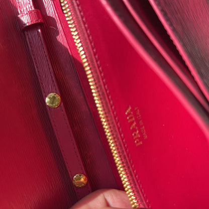 Close-up of a bright pink-red leather clutch or wallet with gold-tone hardware, a gold zipper, and gold-embossed branding on the interior flap.