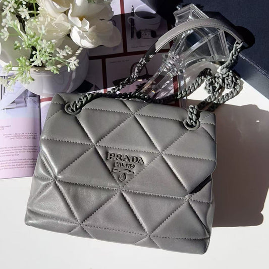 Gray quilted handbag with chain detail on a white surface with flowers 