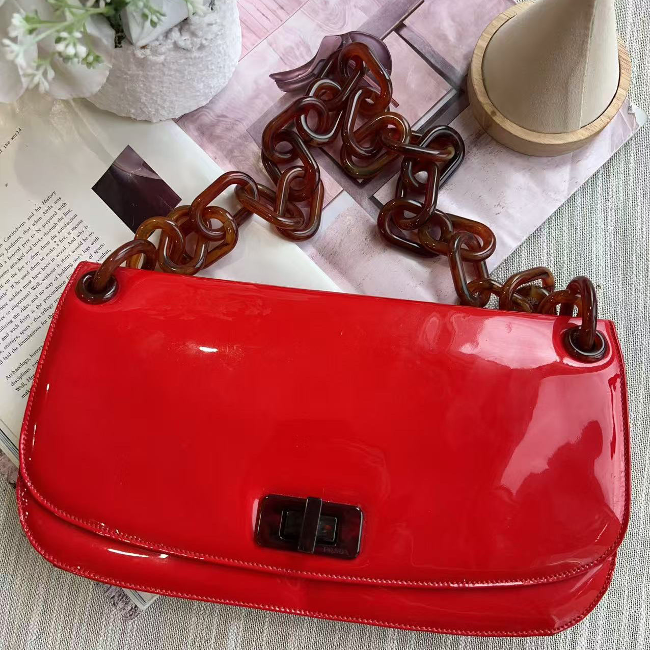 Red handbag with a brown chain strap on a textured surface