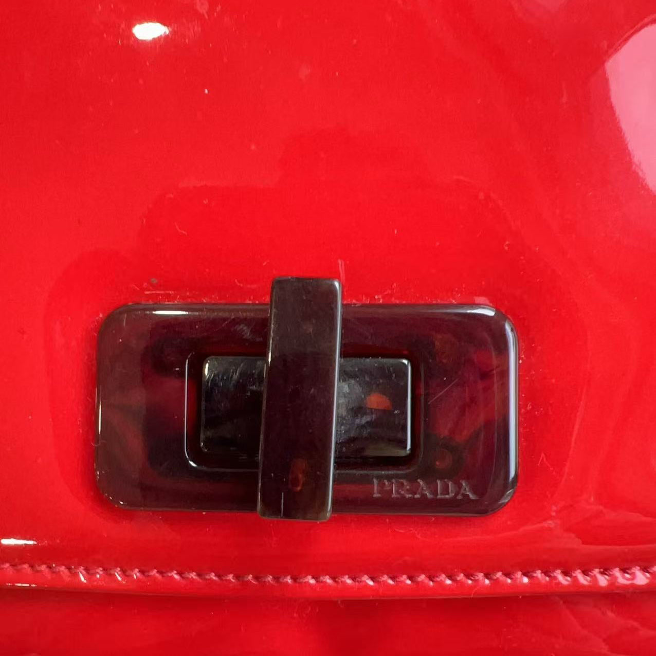 Close-up of a red Prada handbag with a silver buckle.