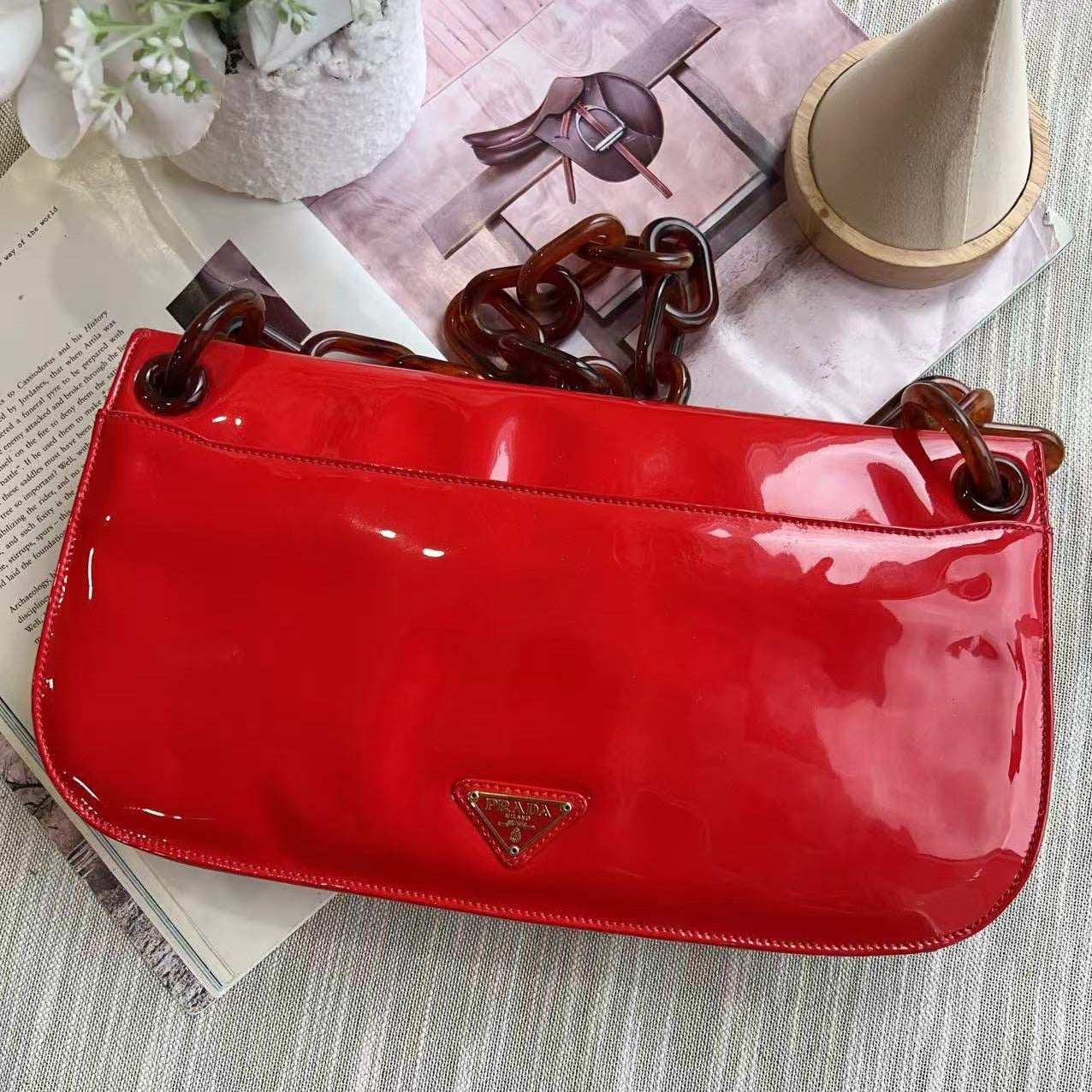 Red patent leather handbag with a brand logo on a light gray surface.