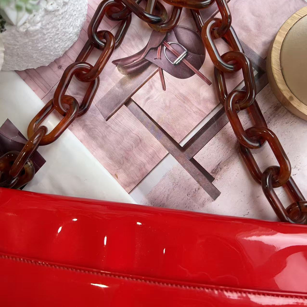 Red handbag with tortoiseshell chain strap on a textured surface