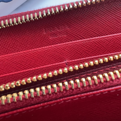 A close-up of a red textured wallet or pouch with gold-tone zippers, showing a faint embossed brand name on the interior.