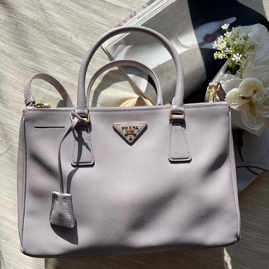 Gray handbag with a brand logo on a wooden surface with flowers.