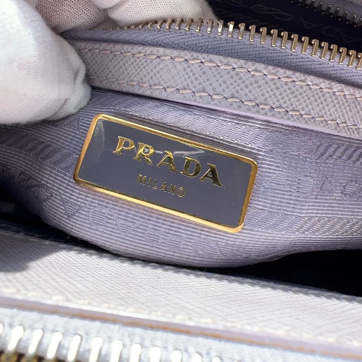 Close-up of a Prada handbag with a gold zipper and visible Prada logo.