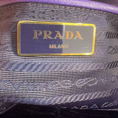 Close-up of a Prada Milano interior label on a purple and navy patterned fabric pouch with gold trim.