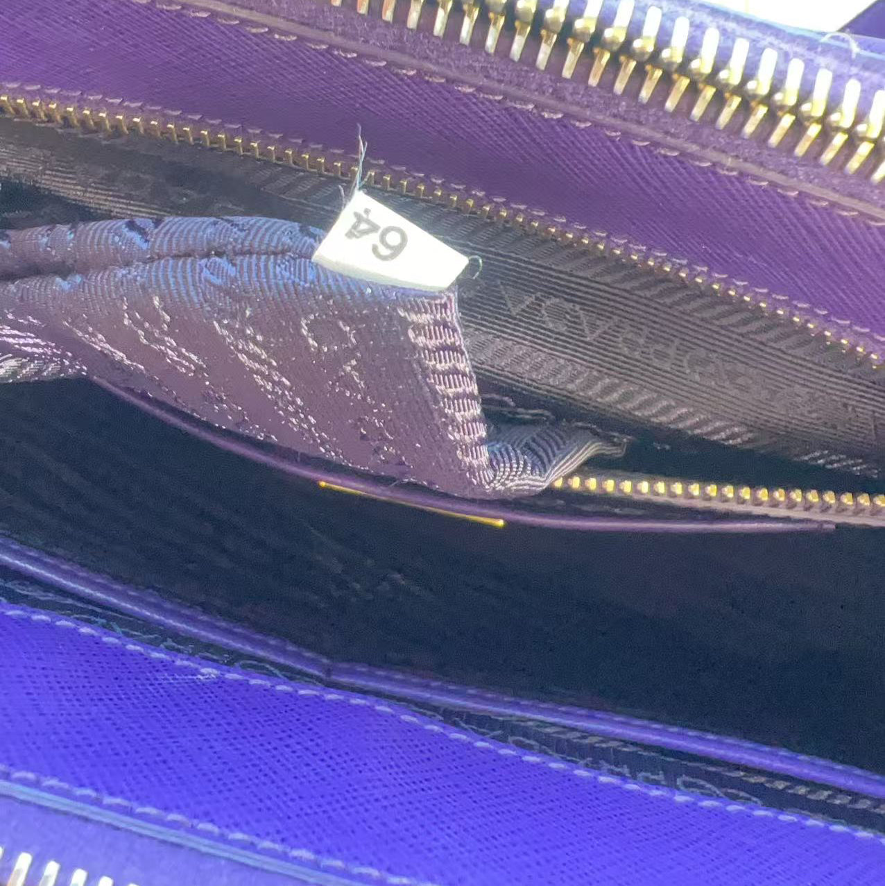 Close-up of an open purple handbag showing the interior lining, a gold-tone zipper, and a small white size tag reading 64.