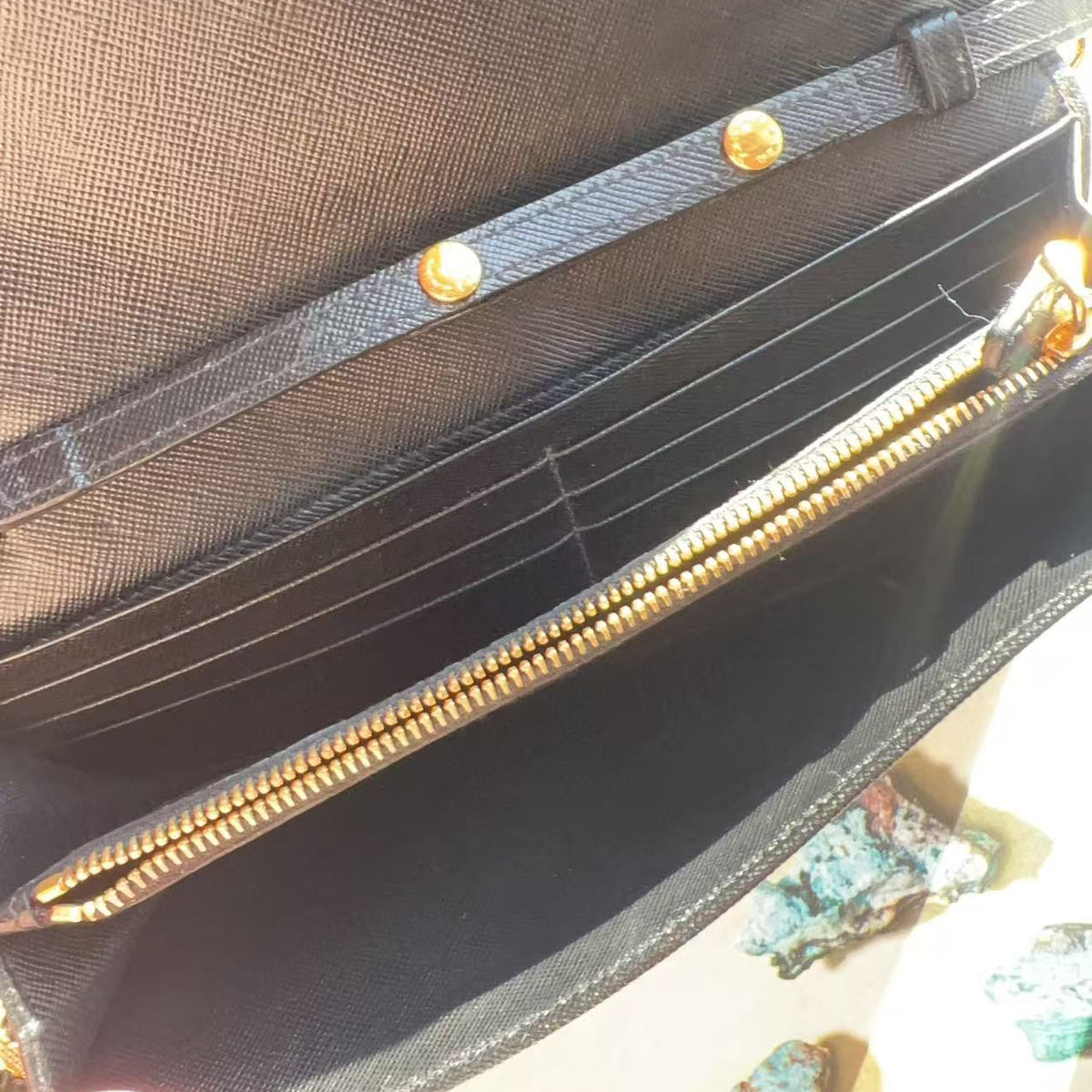 Close-up of a black textured leather or canvas wallet with multiple card slots, a zippered compartment, and gold-tone hardware.
