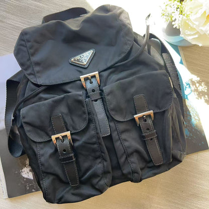 A black nylon Prada shoulder bag with multiple front pockets, brown leather straps, and gold-tone buckles, resting on a light wood surface.