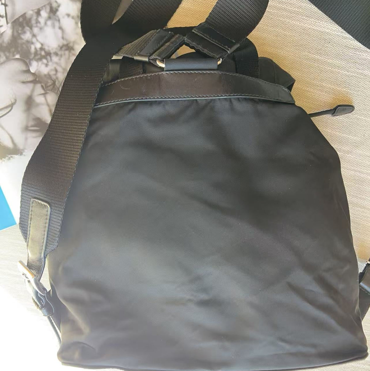 A black nylon messenger bag with a wide adjustable shoulder strap, resting on a light-colored wooden surface.