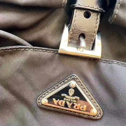 Close-up of a Prada nylon bag with a triangular metal logo plaque and a leather strap with a silver buckle.
