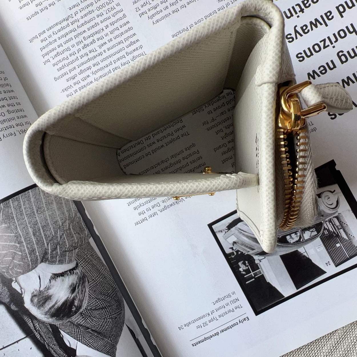 A cream-colored canvas zippered pouch with a gold zipper, shown open and resting on top of an open book.
