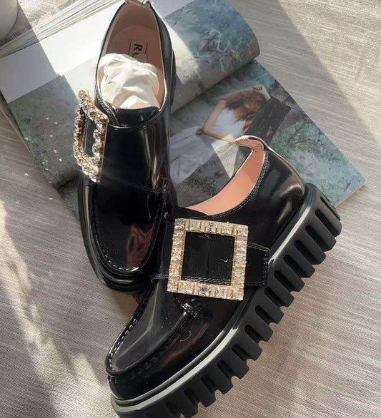 Black platform shoes with decorative buckles on a textured surface