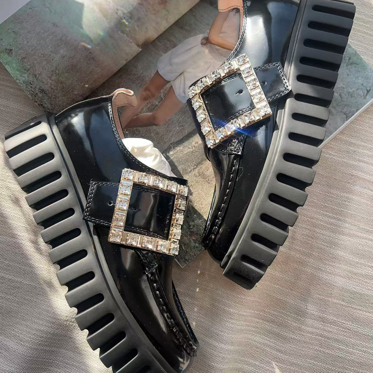 Black platform shoes with square embellishments on a reflective surface