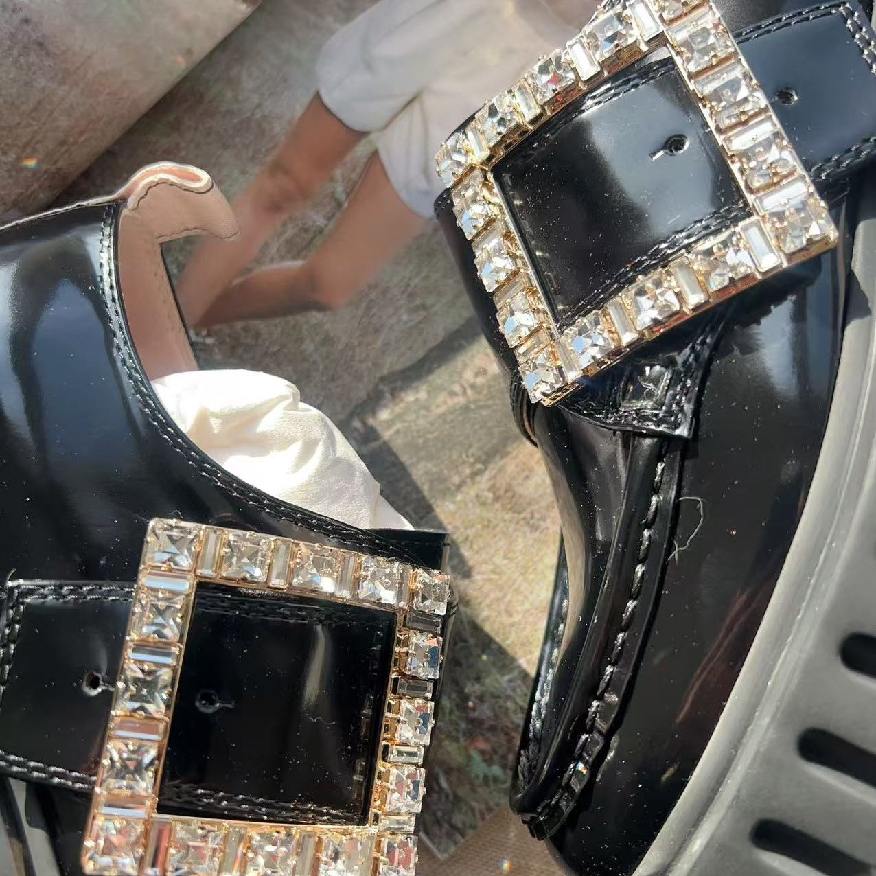 Black shoes with decorative buckles worn by a person on a blurred background