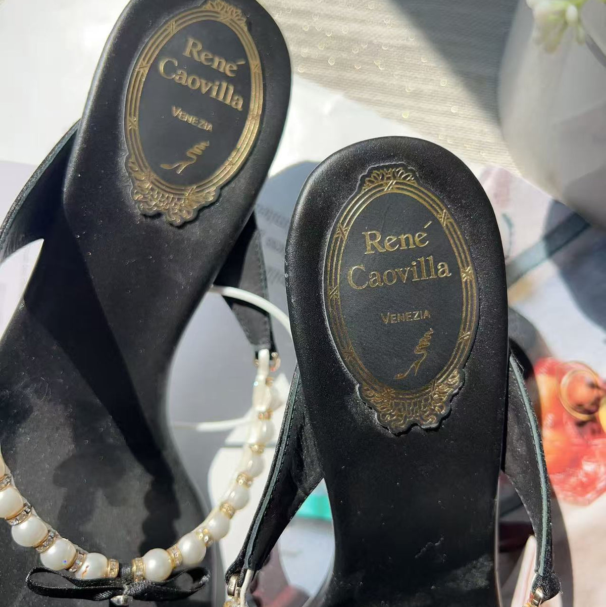Black slingback flat sandals with a pearl strap and gold-tone hardware, shown from the sole side with the Rene Caovilla logo visible.