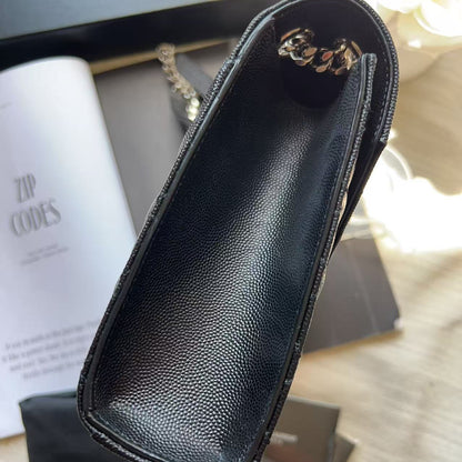 A black Saint Laurent leather pouch with a pebbled texture, shown from an overhead angle with its branded dust bag, box, and instruction booklet on a wooden surface.