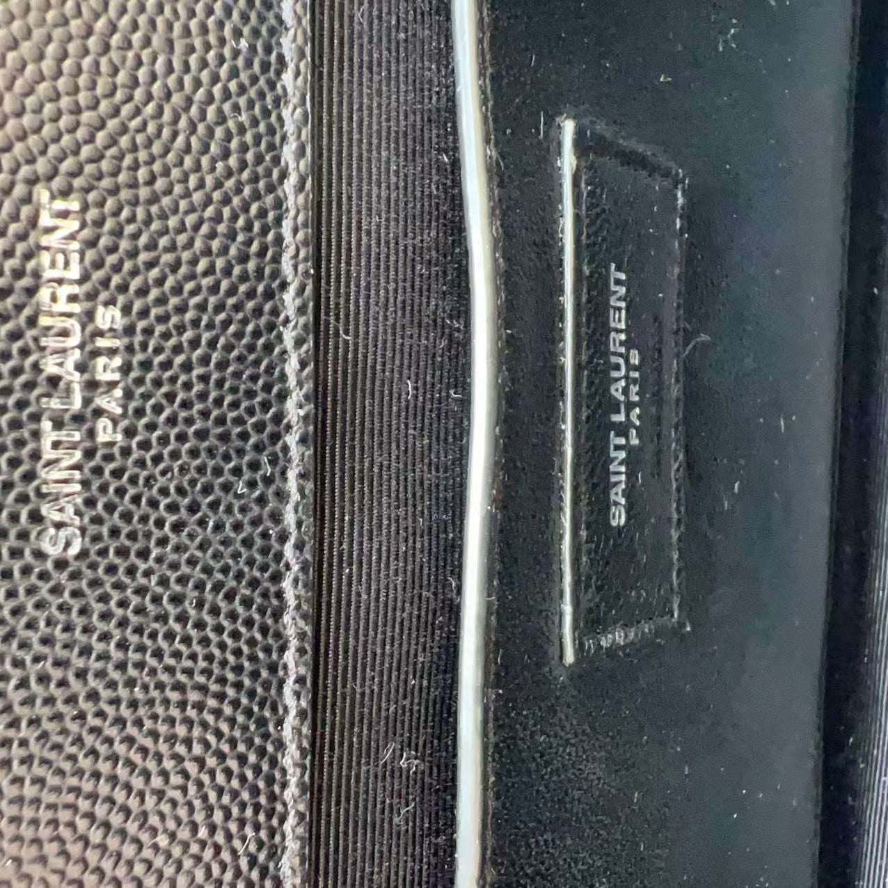 Close-up of a Saint Laurent Paris bag showing textured black leather with debossed vertical branding and a black fabric strap section.