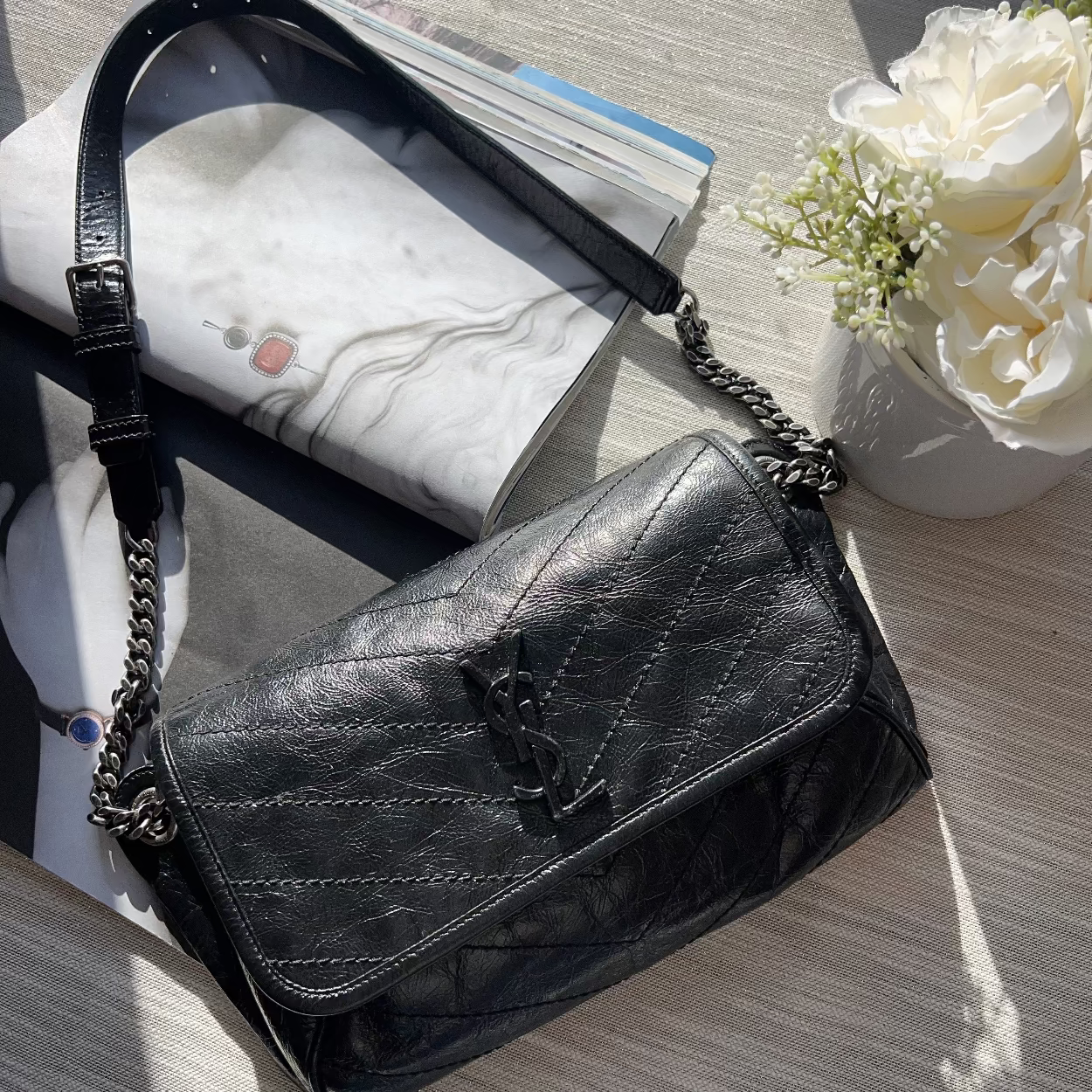 Black handbag on a marble surface with flowers and a magazine