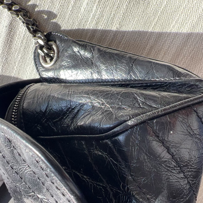 Close-up of a black leather handbag with visible wear on a textured surface
