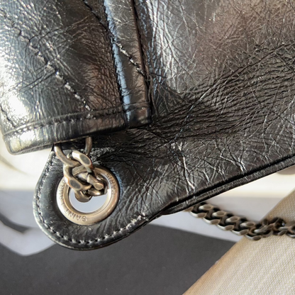 Close-up of a textured black leather handbag with a gold chain detail.