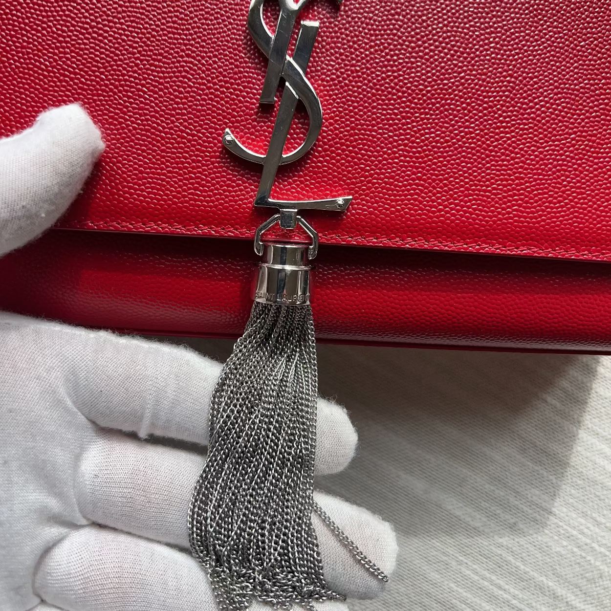 Red handbag with a silver tassel and logo, held by a gloved hand.
