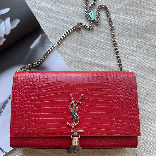 Red handbag with a chain strap on a light wooden surface