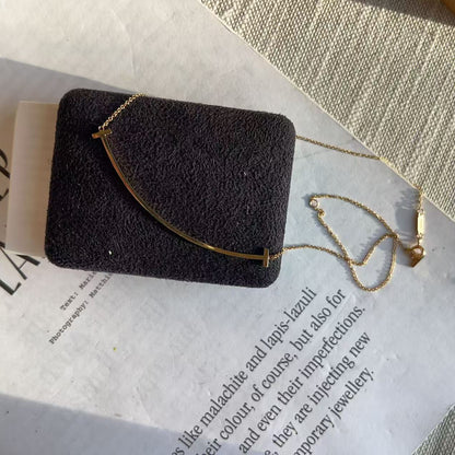 A gold-toned bar necklace displayed on a black textured jewelry stand, placed on top of printed paper with a woven fabric surface in the background.