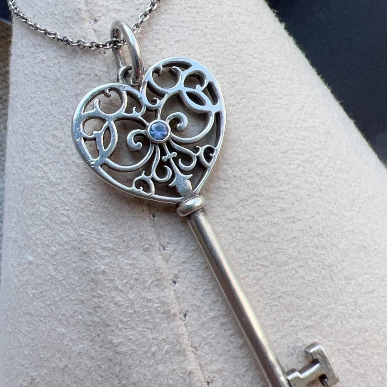 Silver key-shaped pendant with intricate design on a light gray surface