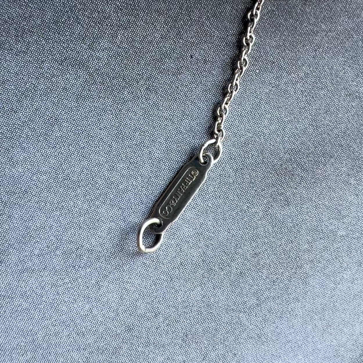 Silver bottle opener with chain on a textured gray background
