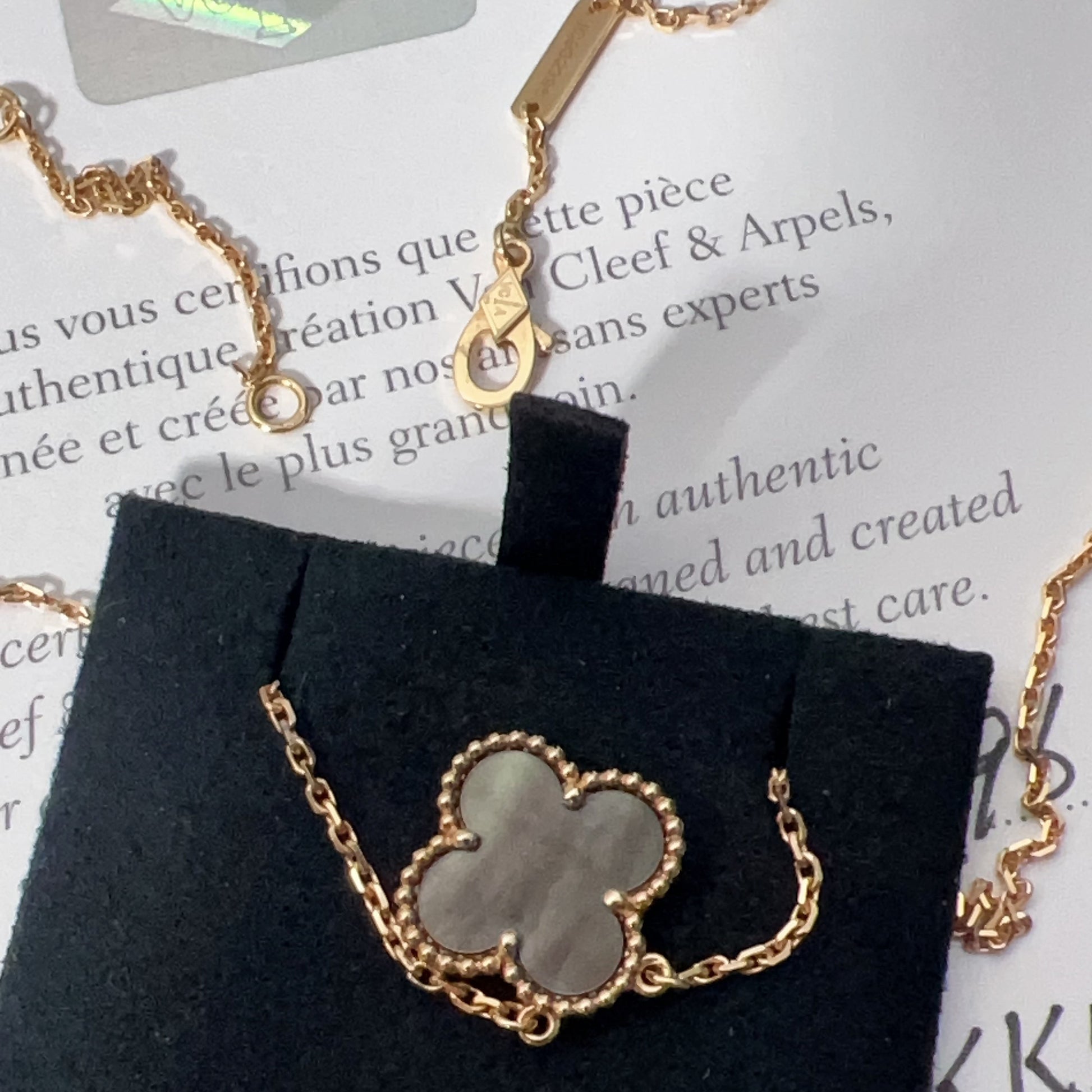 Gold necklace with a clover-shaped pendant on a black display card, with text in the background.