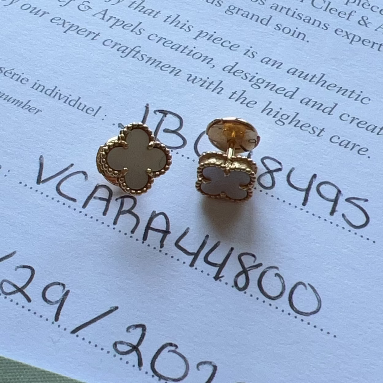 Gold and white clover-shaped earrings on Van Cleef & Arpels certification paper.