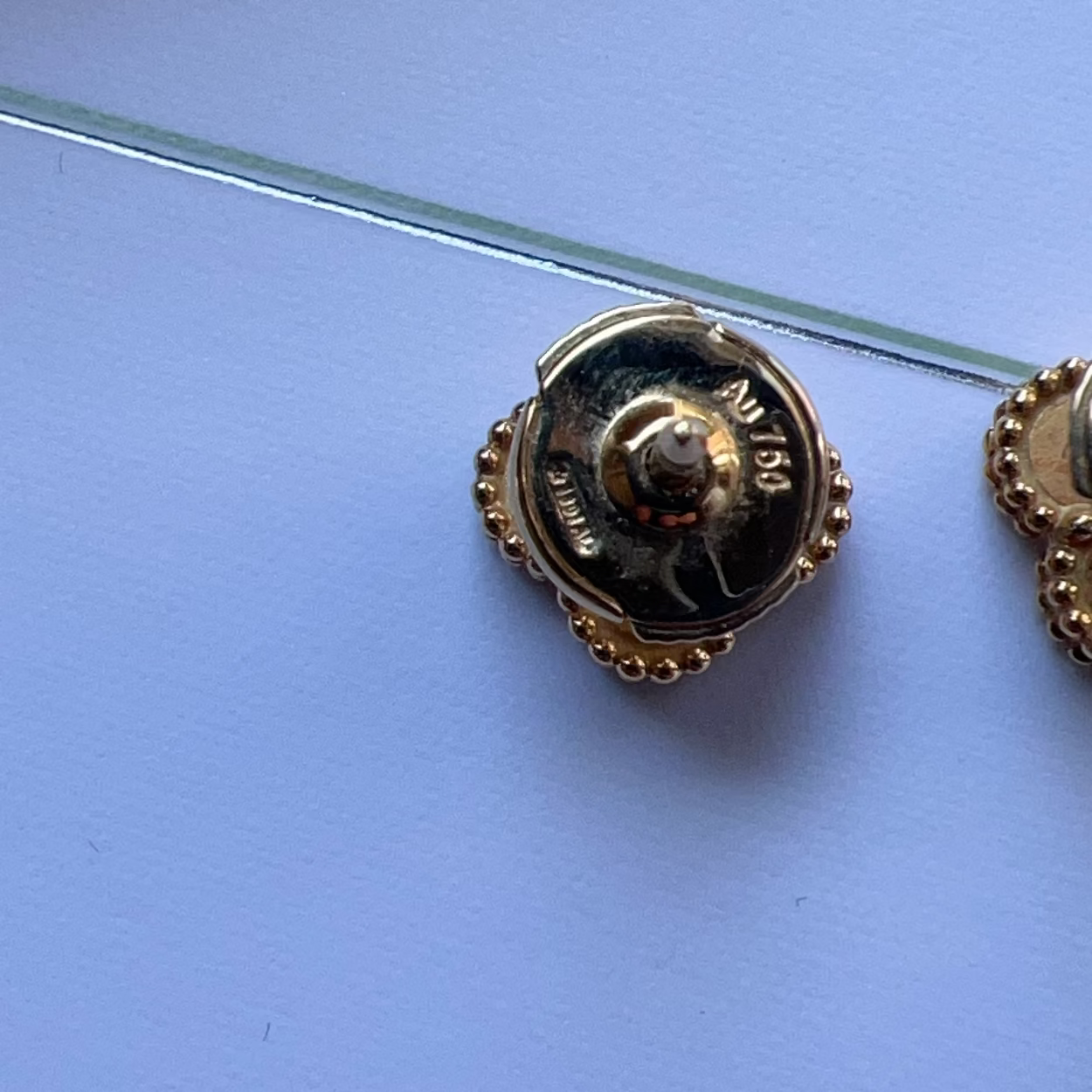 Gold brooch on a clear stand against a blue background