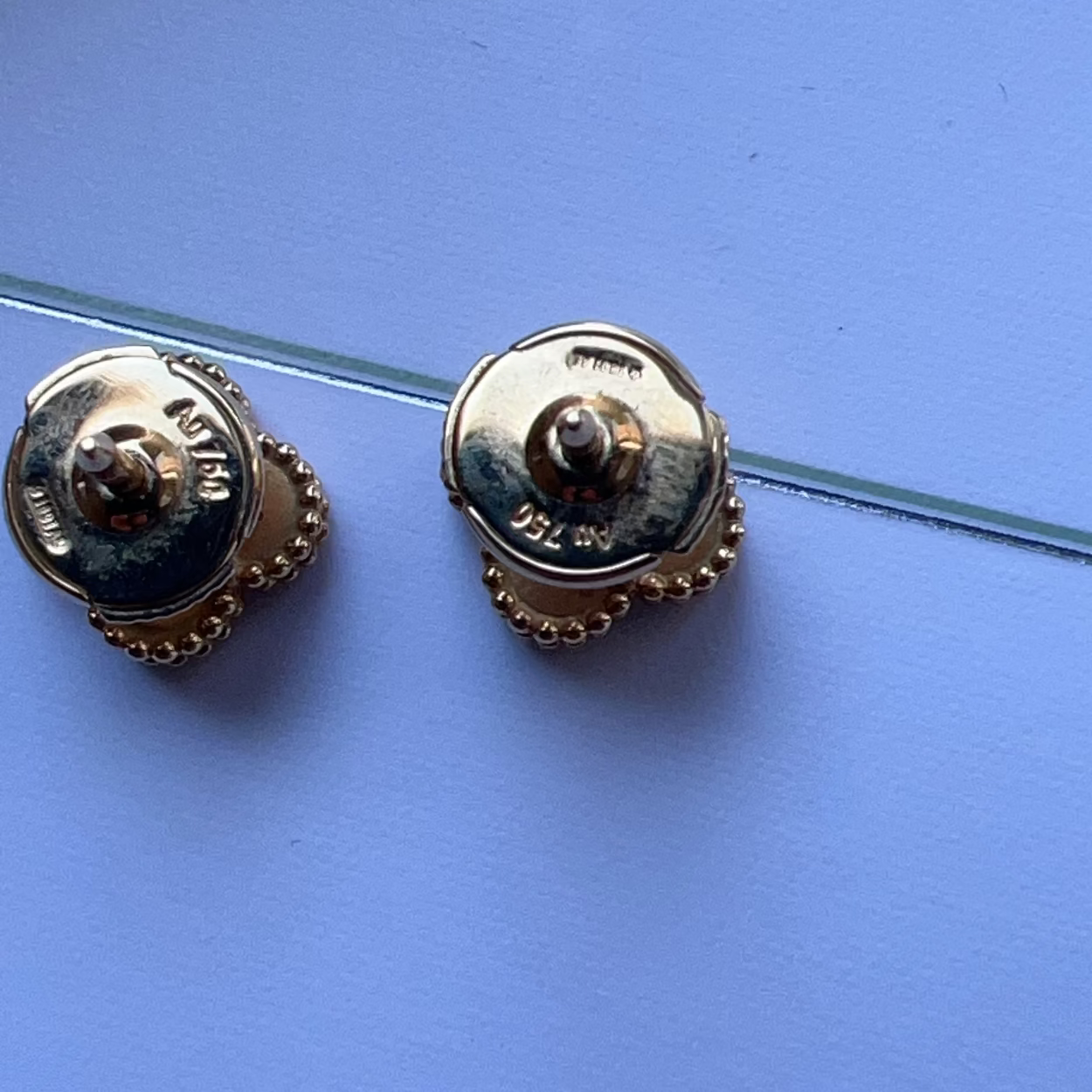 Gold earrings on a clear stand against a blue background