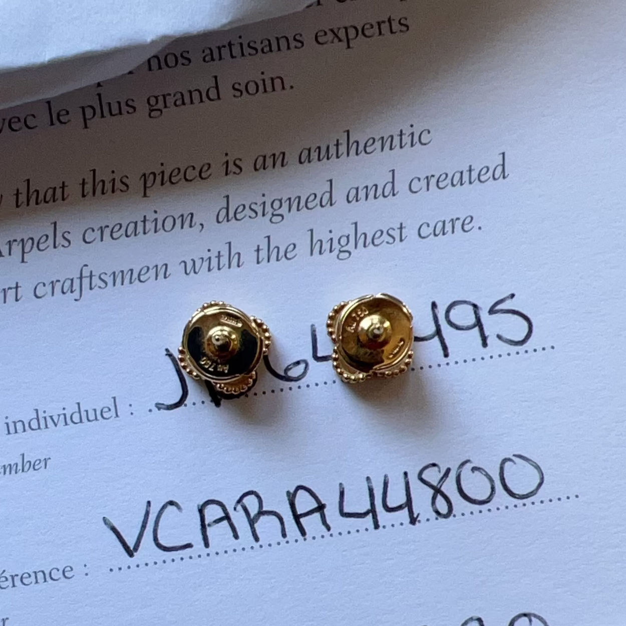 Gold earrings on a piece of paper with text and numbers