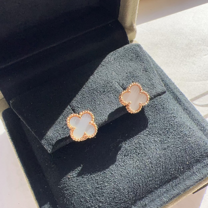 A pair of four-leaf clover stud earrings with white mother-of-pearl centers and rose gold borders, displayed on a black velvet jewelry box.