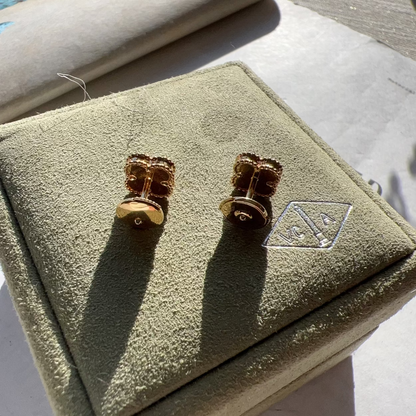 A pair of gold-toned cufflinks displayed on a textured olive-green jewelry box, photographed in bright natural sunlight on a light surface.