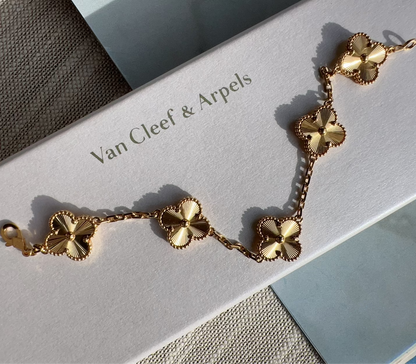A gold-tone Van Cleef & Arpels Alhambra five-flower bracelet displayed on its white branded box, set against a neutral textured background.