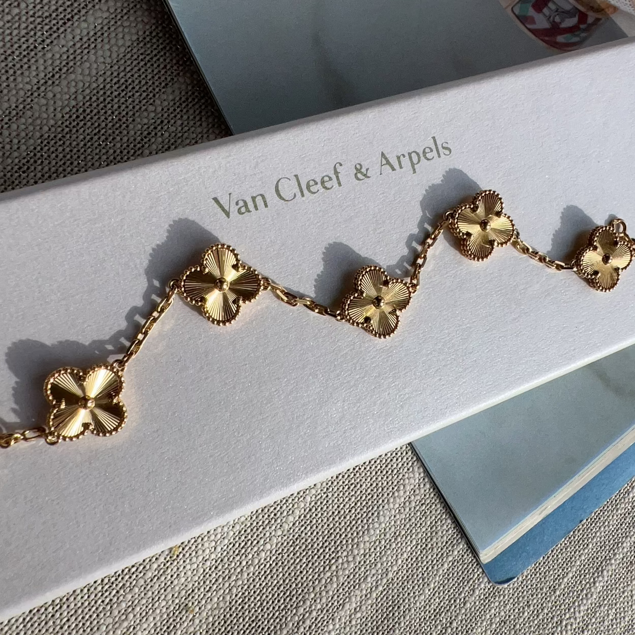 A gold-tone Van Cleef & Arpels bracelet with five clover motifs, displayed on its white branded box.