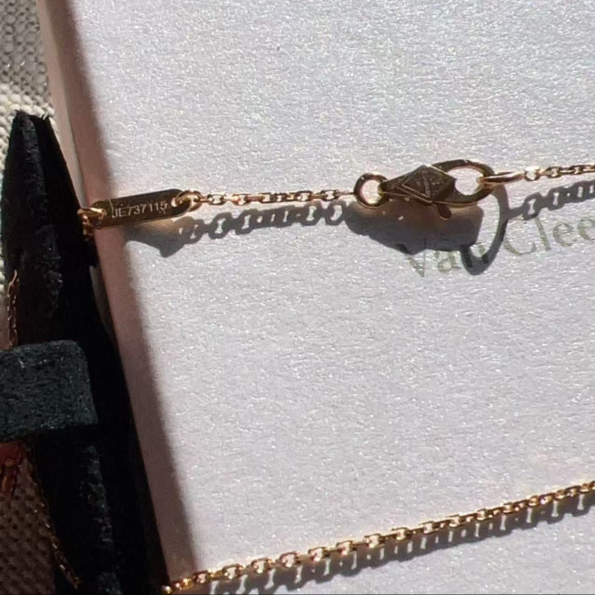 A close-up of a delicate gold chain bracelet with a diamond-shaped clasp resting on a white jewelry box. The brand name 'Van Cleef' is partially visible on the box, and the inside of the clasp shows the engraving 'VAC 137110'.