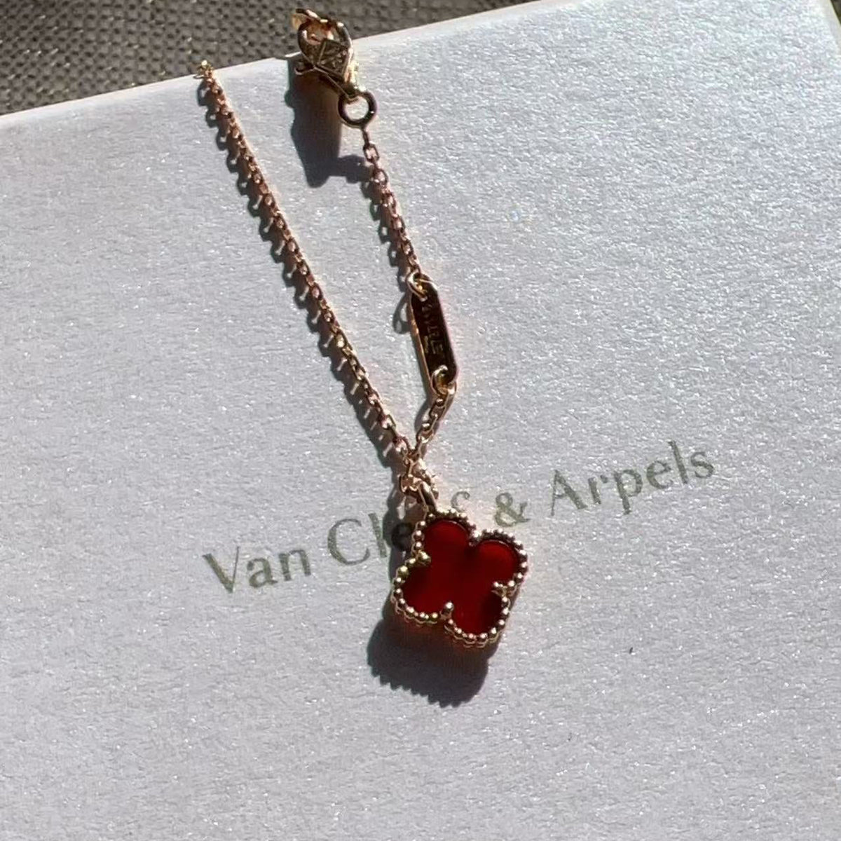 A gold-tone chain necklace with a red four-leaf clover pendant, resting on a white Van Cleef & Arpels box.