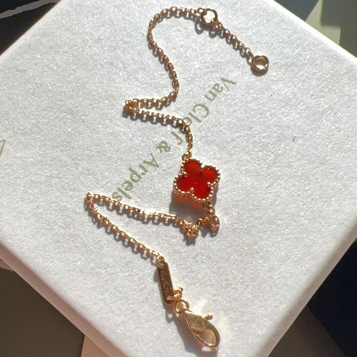 A gold-toned Van Cleef & Arpels Alhambra-style four-leaf clover necklace with a red cabochon center, displayed on a white branded jewelry box.