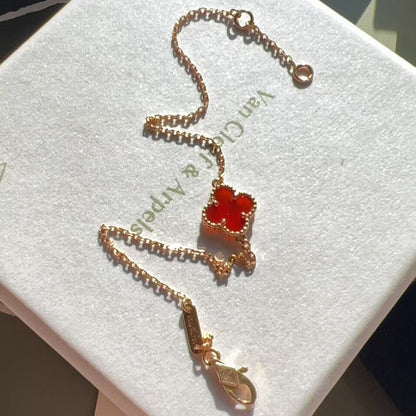 A gold-toned Van Cleef & Arpels Alhambra-style four-leaf clover necklace with a red cabochon center, displayed on a white branded jewelry box.