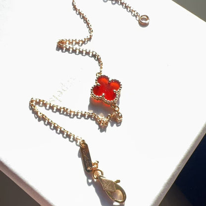 A gold-tone chain necklace with a red four-leaf clover pendant and a matching gold clasp, displayed on a white jewelry box.