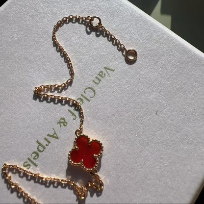 A gold-toned Van Cleef & Arpels Alhambra necklace with a red enameled four-leaf clover pendant, resting on a white branded jewelry box.