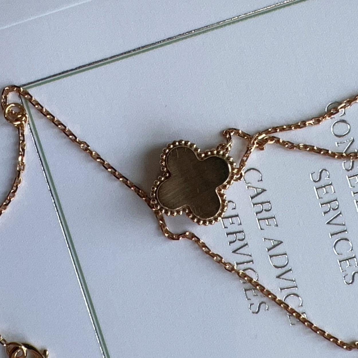 Gold necklace with a clover-shaped pendant on a white card with text.