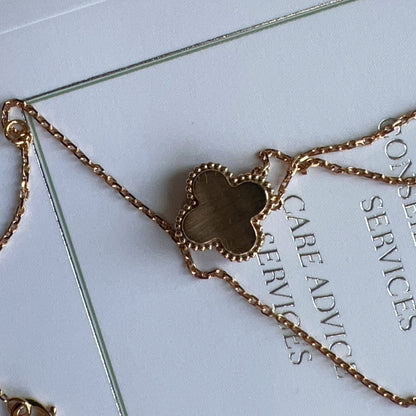 Gold necklace with a clover-shaped pendant on a white card with text.