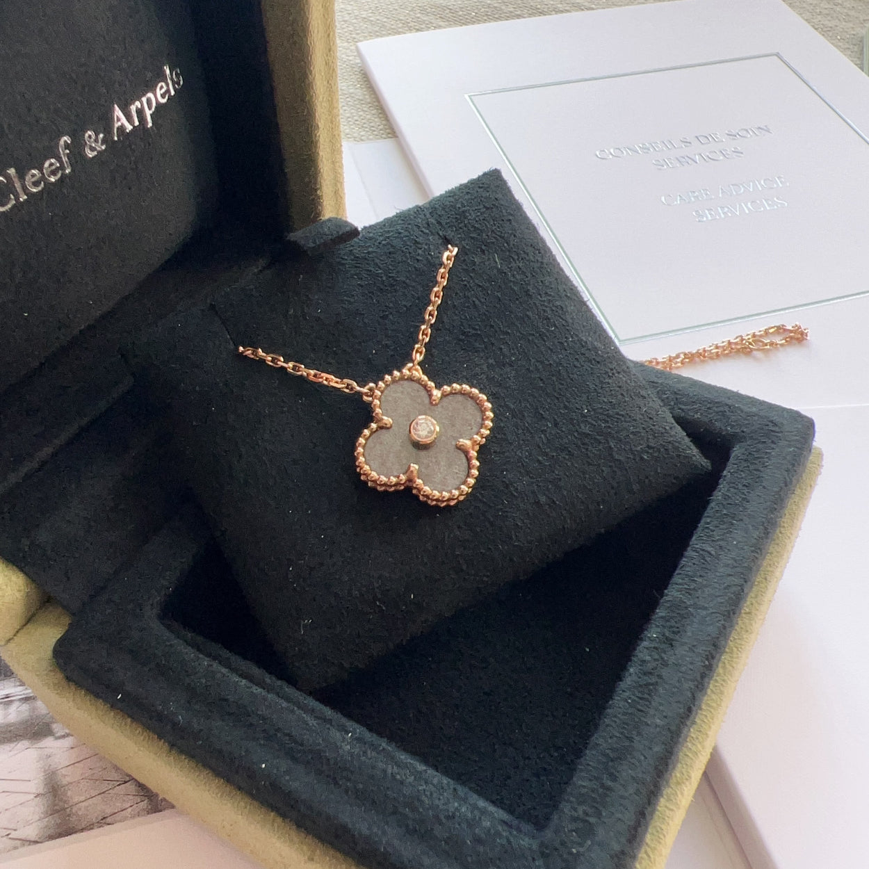 Flower-shaped necklace in a Cleef & Arpels box on a wooden surface.